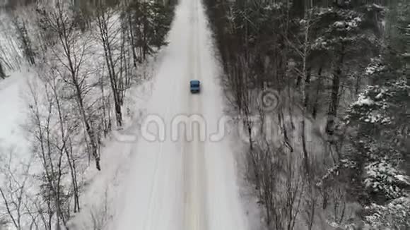 蓝色复古汽车在森林里的冬季乡村道路上行驶空中观景台视频的预览图