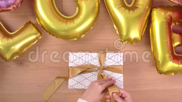一位穿着白色毛衣的年轻女士正在包装用金色气球包装漂亮的礼品盒准备节日准备视频的预览图