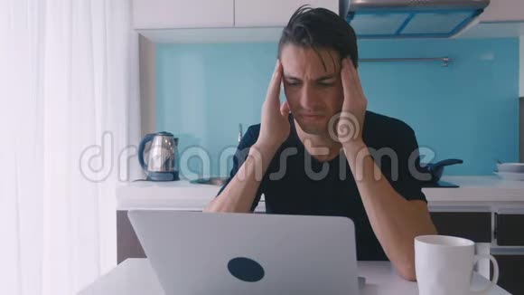 沮丧的年轻人在厨房里用笔记本电脑工作时感到痛苦和头痛视频的预览图