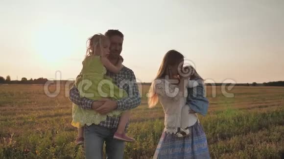 日落时分年轻的父母抱着孩子穿过田野视频的预览图