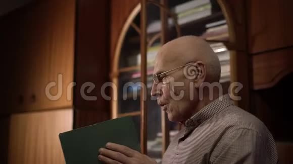 戴眼镜的老人拿着一本绿色的大书吹着灰尘视频的预览图