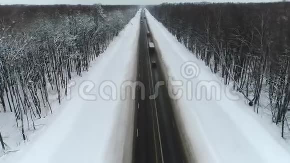 冬季驾驶的汽车和卡车的空中飞行道路被雪和树包围视频的预览图