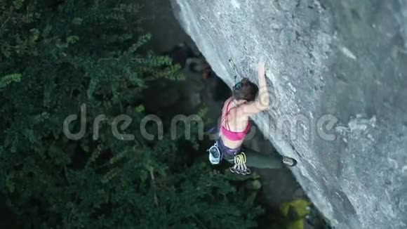 女子攀岩者在艰难的运动路线上攀爬完成拿着顶链和夹绳视频的预览图
