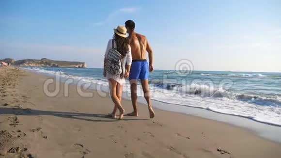 一对情侣在海边散步在度假胜地休息时牵手男人拥抱女人漫步在海滩上视频的预览图