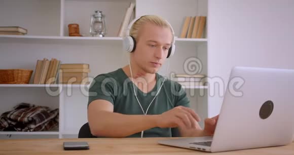 年轻英俊的金发时髦商人戴着耳机在办公室里轻松地使用笔记本电脑的特写肖像视频的预览图
