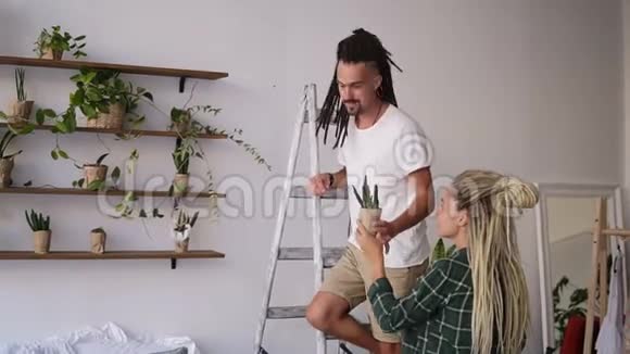 一对年轻夫妇在一起整理家务站在梯子上把植物放在架子上的人他的美丽视频的预览图