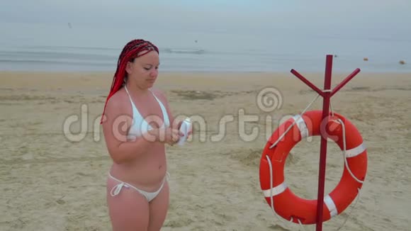 一位身穿白色泳衣的年轻女子在海滨的身上涂防晒霜视频的预览图