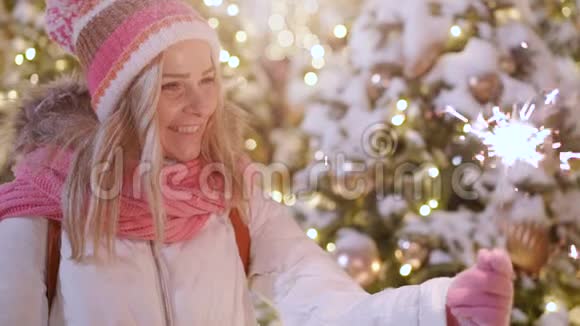 美丽的微笑女孩拿着火花在街上摆姿势背景上有冬天的灯光视频的预览图