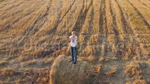 一个少年站在干草堆上挥着手户外娱乐乡村日落视频的预览图