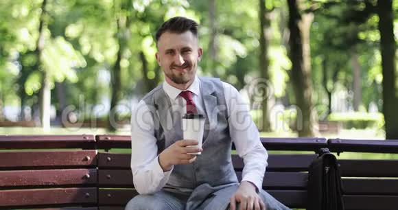 白人看起来不错的商人在夏天公园喝咖啡视频的预览图