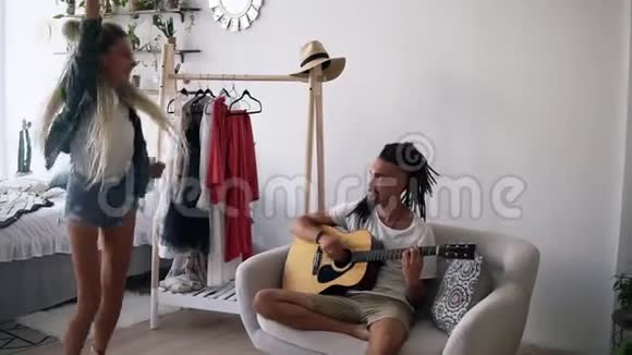 男人和女人在家玩得开心坐在沙发上弹吉他的家伙他女朋友在跳舞视频的预览图