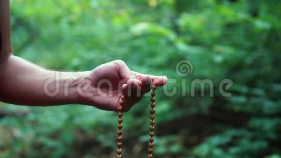 手中的祈祷珠男性手拿念珠向上帝祈祷绿色自然背景宗教灵性视频的预览图