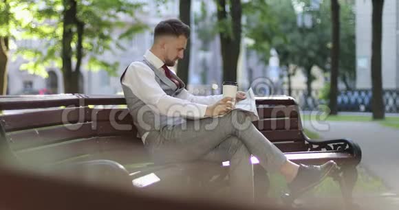 一个穿着昂贵西装的商人坐在公园的长凳上看报纸视频的预览图