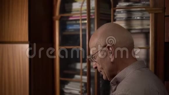 戴眼镜的退休秃头从书架上拿走了一大本旧书视频的预览图