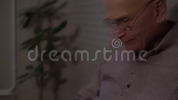 戴眼镜的微笑老人坐在扶手椅上拿着照片视频的预览图