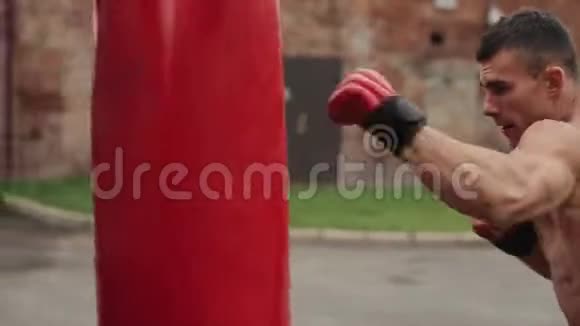 近距离观看穿红色手套的男拳击手在户外打红色拳击袋视频的预览图