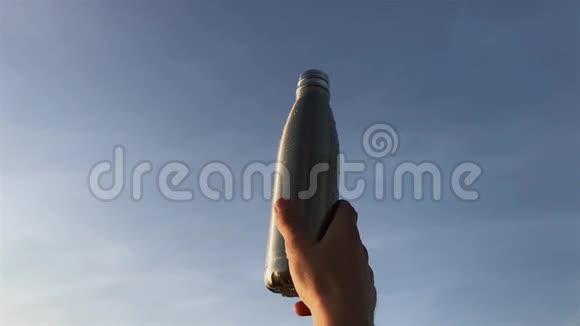 在蓝天背景下男性手握钢制热水生态瓶视频的预览图