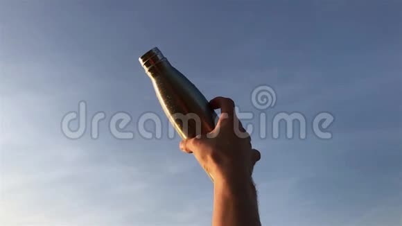 在蓝天背景下男性手握钢制热水生态瓶视频的预览图