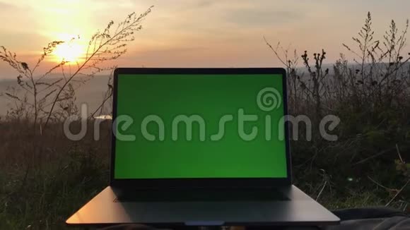 现代笔记本电脑的特写背景是日落的绿色屏幕视频的预览图