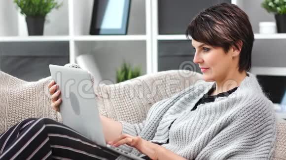 微笑美丽的成熟女性在舒适的家里放松用笔记本电脑媒体特写聊天视频的预览图