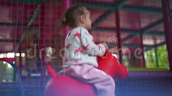 一个可爱的小白种人女孩在操场上玩耍夏天骑着一匹橡胶马视频的预览图
