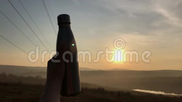 在日落背景下用男性手握钢制生态热瓶进行水的特写视频的预览图