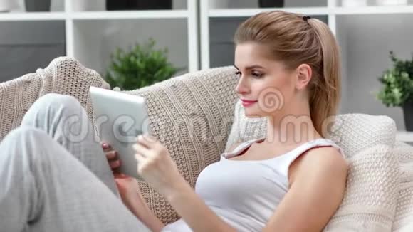 迷人的金发女郎微笑着看着平板电脑屏幕在家放松中特写视频的预览图