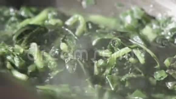 在平底锅里用大蒜煎的菊苣蔬菜和在蒸煮过程中混合的木勺的特写镜头视频的预览图
