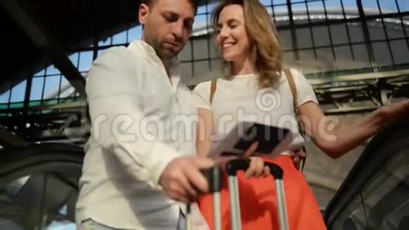 年轻快乐的一对夫妇在夏天的时候带着行李登上了通往机场出发区的自动扶梯视频的预览图