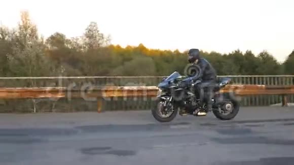 戴头盔的摩托车手骑着现代运动摩托车在公路上生锈的旧桥上疾驰年轻人在比赛视频的预览图