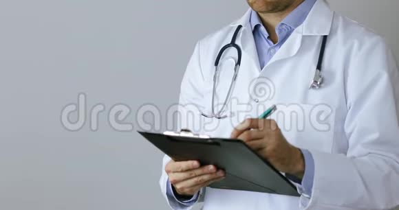 白大褂医生在灰色背景的剪贴板上写文件视频的预览图