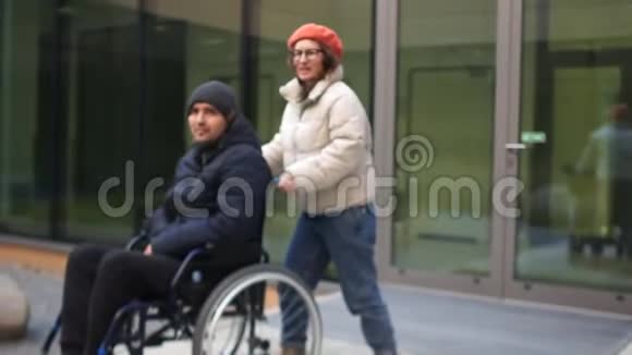 女人带着一个年轻人坐轮椅一对年轻夫妇穿着秋天的夹克和帽子残疾人及其视频的预览图