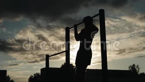 一个强壮的年轻人在街头锻炼时在水平杆上做拉力运动的剪影从底部看日落的天空视频的预览图