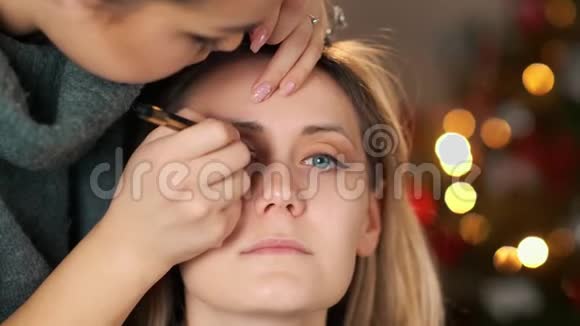化妆师化妆用钢笔画眼线在圣诞节气氛的背景下视频的预览图