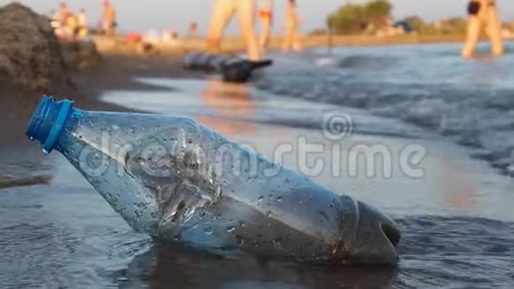 一个塑料瓶躺在海滩上波浪在上面冲刷特写慢动作与环境作斗争的概念视频的预览图