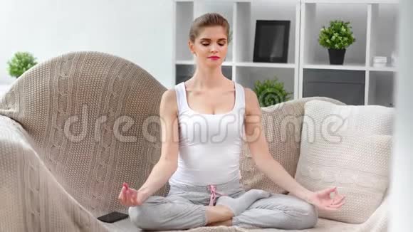 家庭微笑女孩练习瑜伽呼吸坐在家里的莲花位置视频的预览图