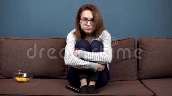 一个戴眼镜的年轻女子紧张地看电视女孩爬上沙发抱着腿视频的预览图