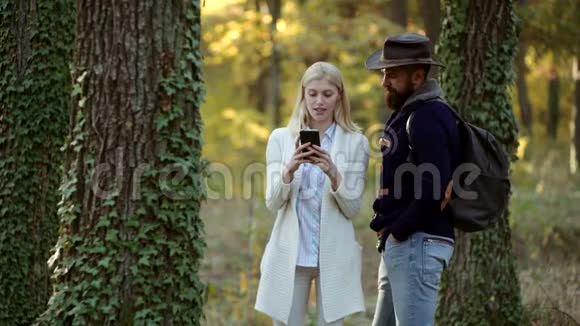 以自然为背景的秋装时装肖像在户外使用智能手机的情侣无忧无虑的秋日情侣视频的预览图