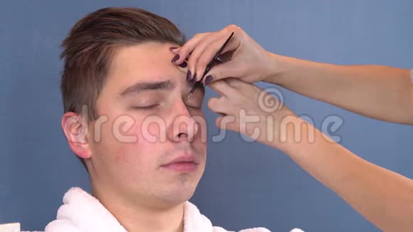 一个年轻人在水疗沙龙里挑眉毛女人镊子抽出眉毛一个穿着白大褂的人视频的预览图