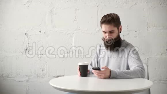 快乐的留胡子的男人坐在桌子旁桌上有电话喝着咖啡视频的预览图