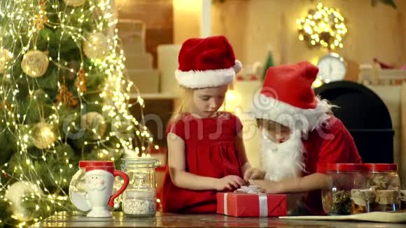 两个戴着圣诞帽的快乐可爱的孩子带着礼物过圣诞节新年圣诞节的概念快乐的孩子抱着视频的预览图