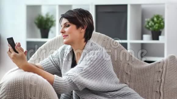 微笑迷人的成熟女性聊天使用智能手机积极的情绪放松在家视频的预览图
