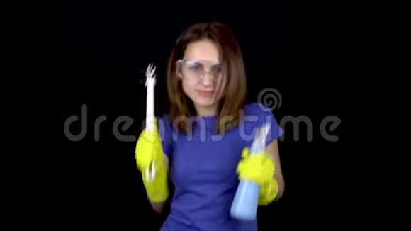 一个年轻的女人正在用马桶刷和喷雾跳舞戴安全眼镜和带清洁工具手套的女人视频的预览图