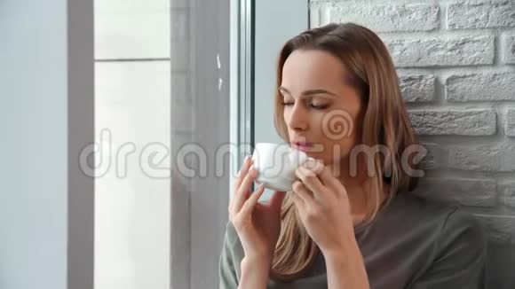 有代表性的家庭年轻女性喝着咖啡透过窗户享受孤独视频的预览图