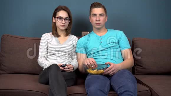 一男一女看电视笑一对年轻夫妇坐在沙发上吃薯片有趣的时刻视频的预览图