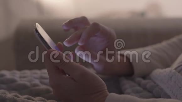 现代概念特写女人双手坐在沙发上用她的智能手机手指放在屏幕上视频的预览图