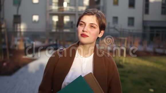 一个穿棕色外套的短发女孩手里拿着一个文件夹一的女商人在一个院子里视频的预览图