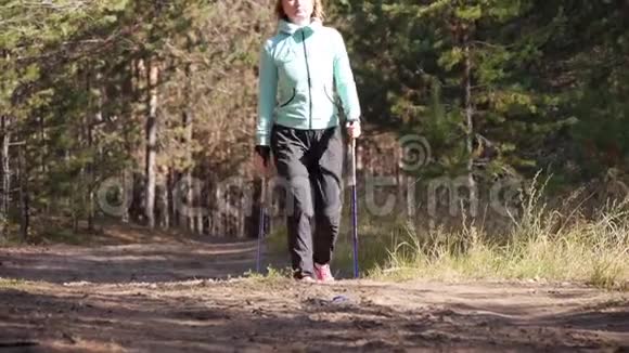 女人练习北欧在秋天的森林里行走她去沙路上的相机正面观点视频的预览图