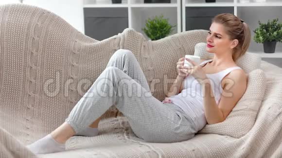 有魅力的年轻女孩在沙发上放松喝茶有积极的情绪享受周末的全镜头视频的预览图