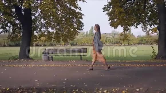秋天一位穿着格子夹克和芥末裙优雅的高加索女人在路上漫步的侧面景色视频的预览图